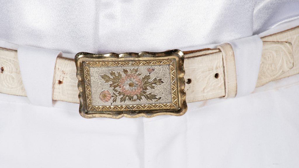 Detail shot of the belt of a country performer's outfit; belt buckle is metal and rectangular with a floral design