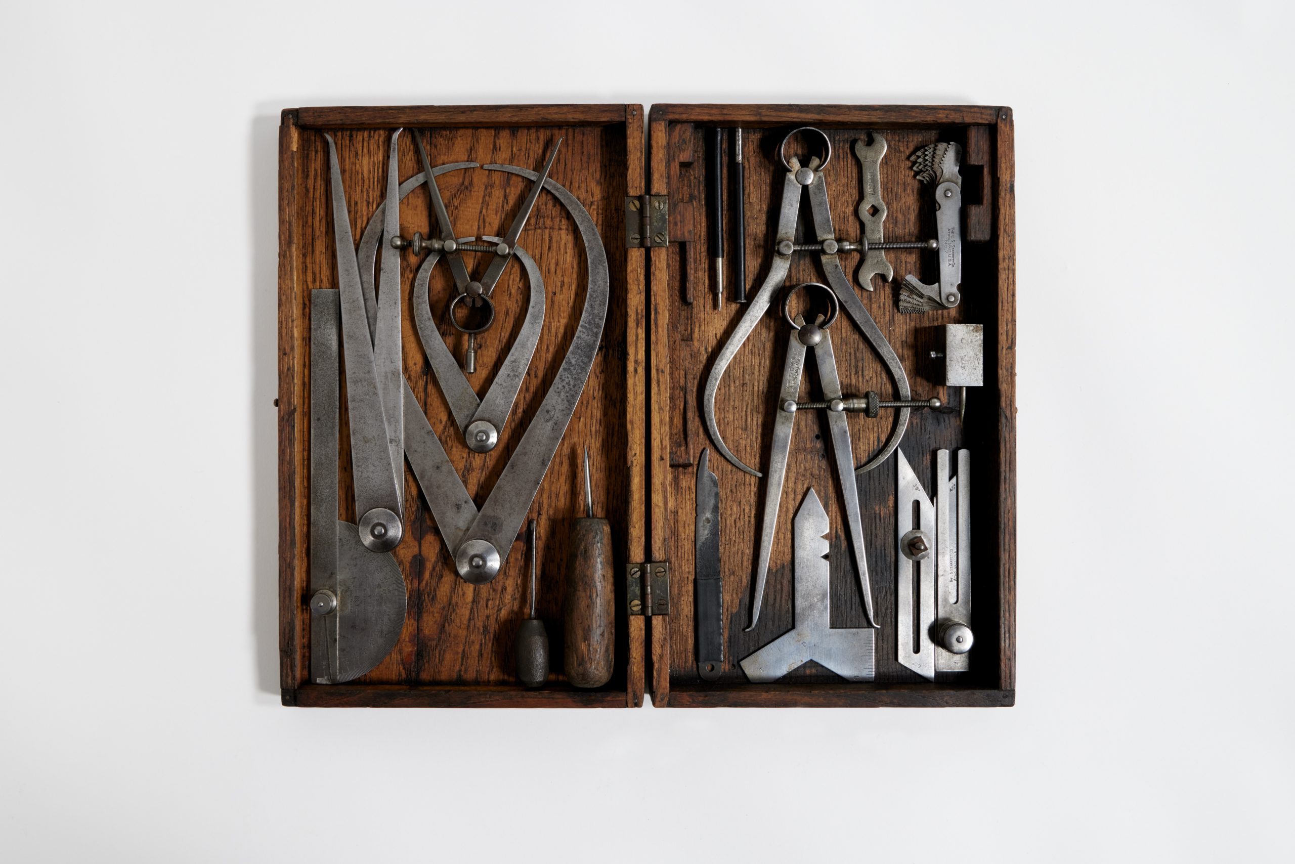 flat wooden case full of metal tools like box cutters, pincers, pens, screwdrivers