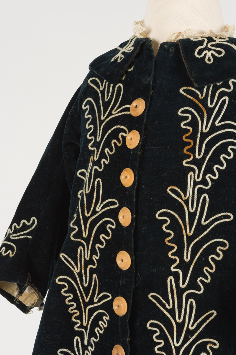 detail of child's coat, it has a small folded collar with embroidered lace rim on the top