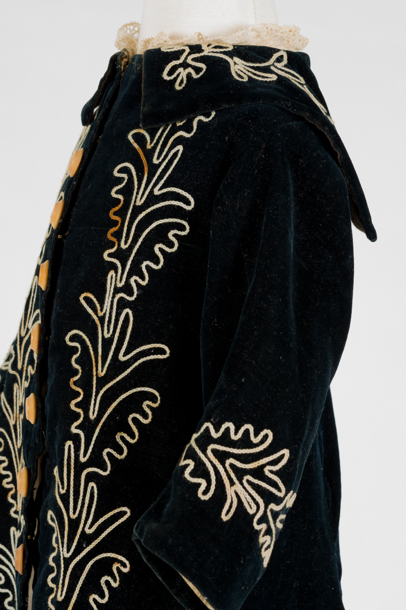 detail of child's coat, the collar extends round the back and is longer to create a small capelet with embroidered detail