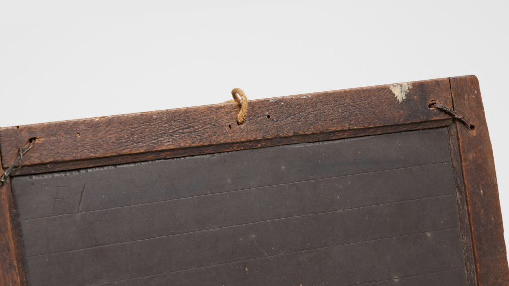 Close up of black writing slate with a damaged wooden frame, including a small string fed through the top