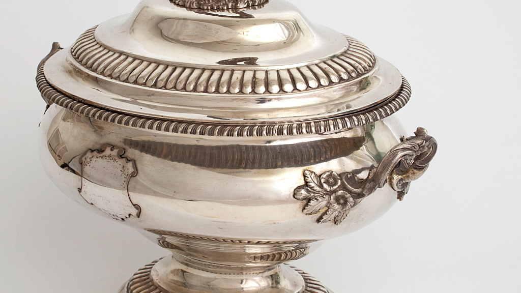 Ornate silver soup tureen embellished with petal shapes, scrolls, and floral fittings, photographed on an angle