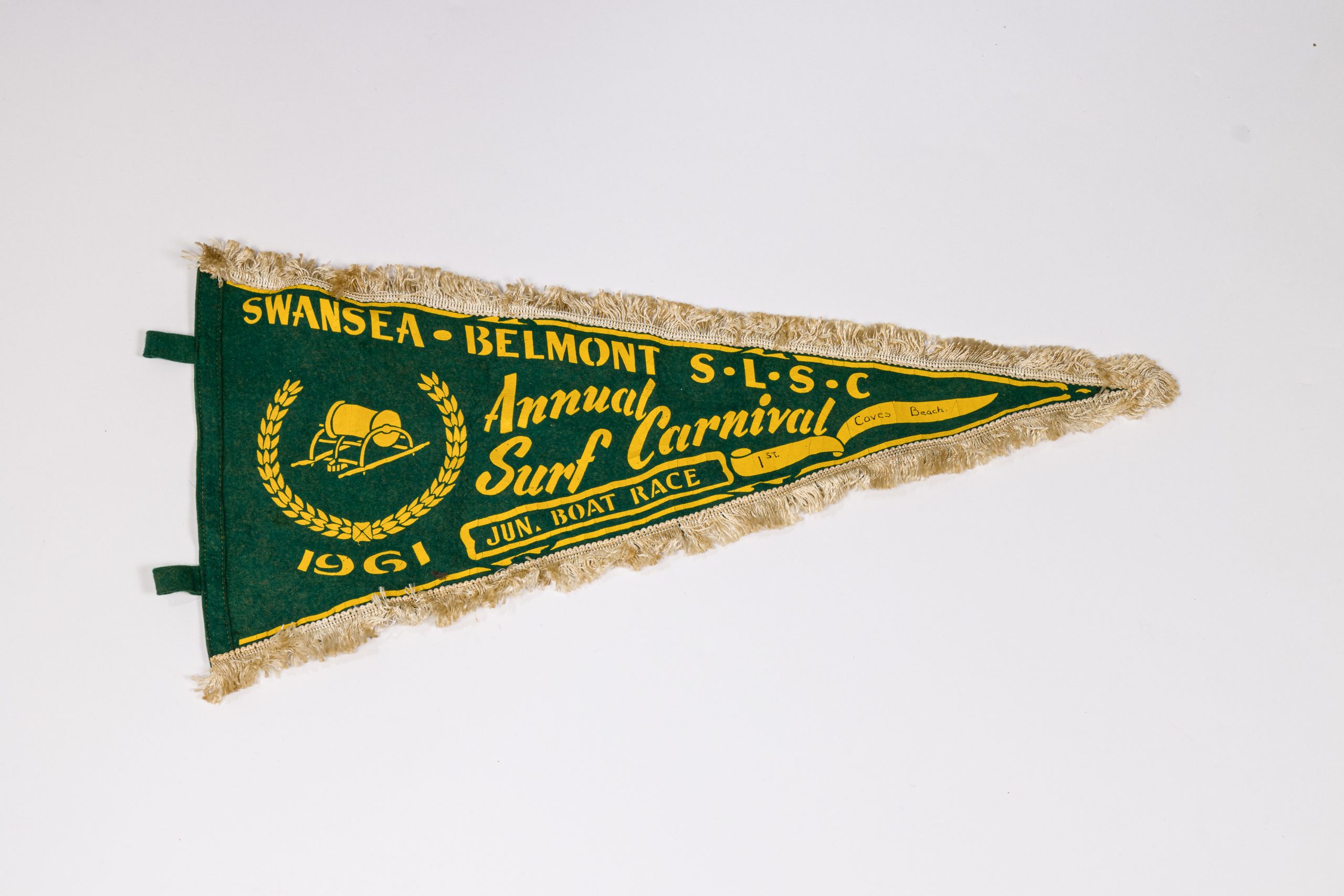 Green and gold pennant with a fuzzy beige trim which reads: "SWANSEA-BELMONT S.L.S.C Annual Surf Carnival 1961 Jun. Boat Race, 1st Caves Beach."