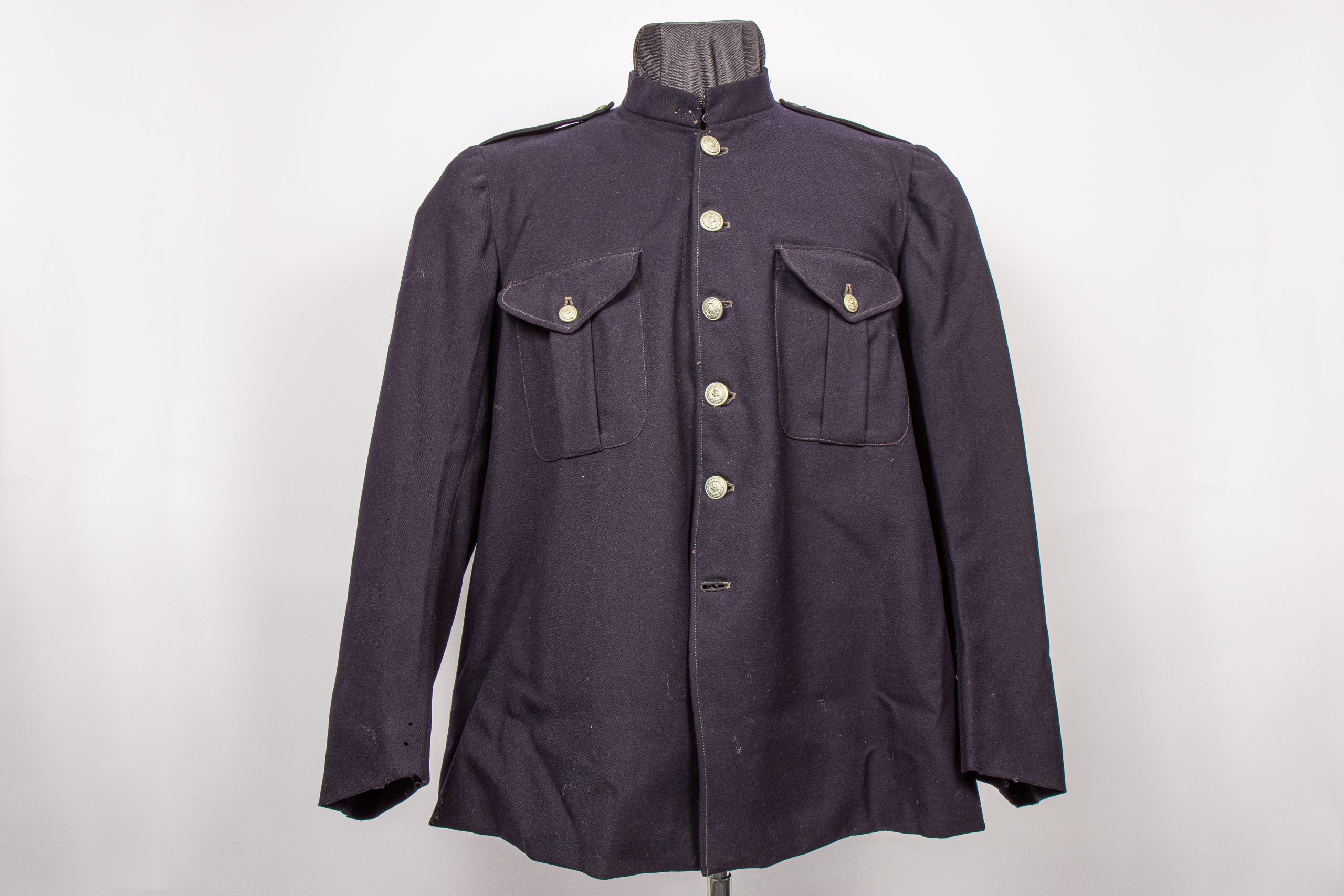 Old police jacket made of dark blue material adorned with five metal buttons and two front pockets, the collar is upturned.
