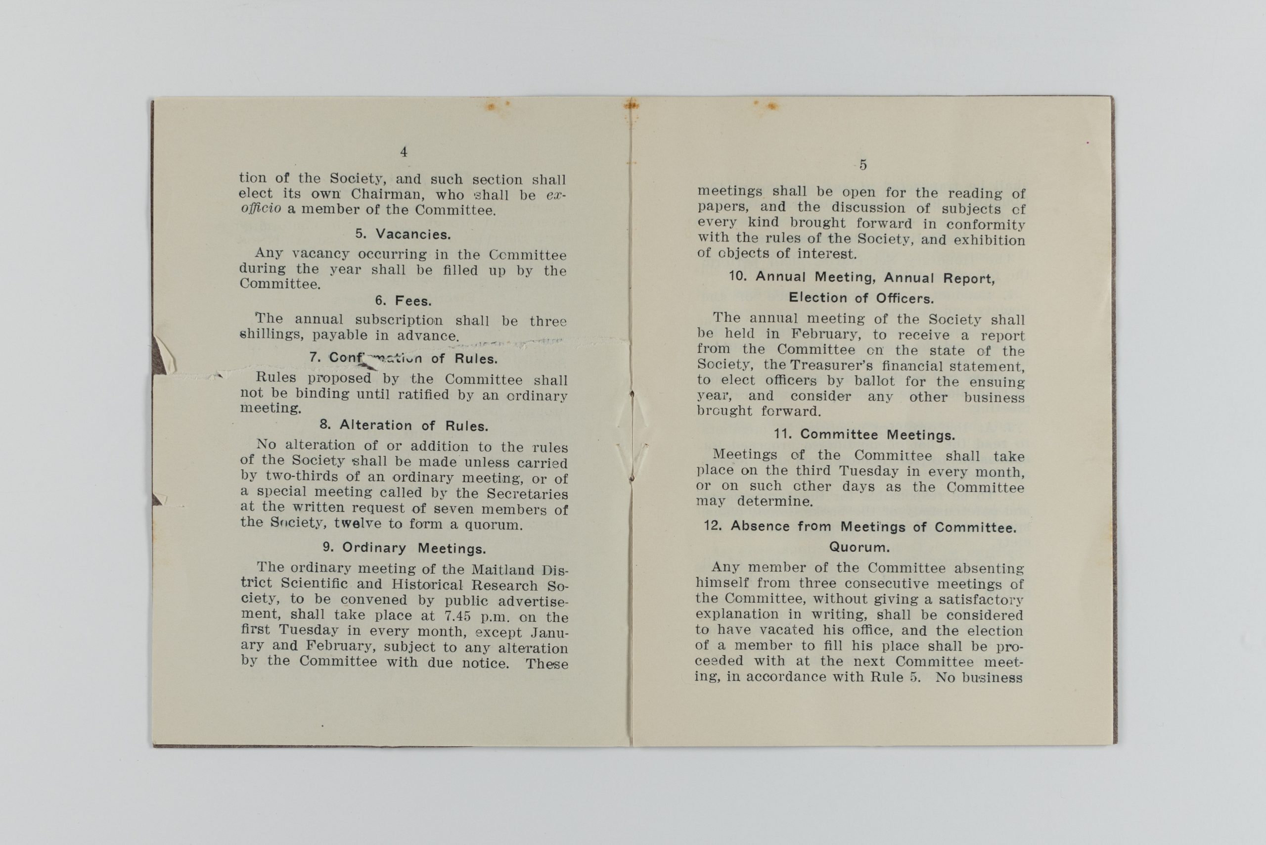 Printed book open to pages showcasing rules 5-12, including vacancies, fees, confirming/altering rules, ordinary/annual/comittee meetings, and absence from such meetings.