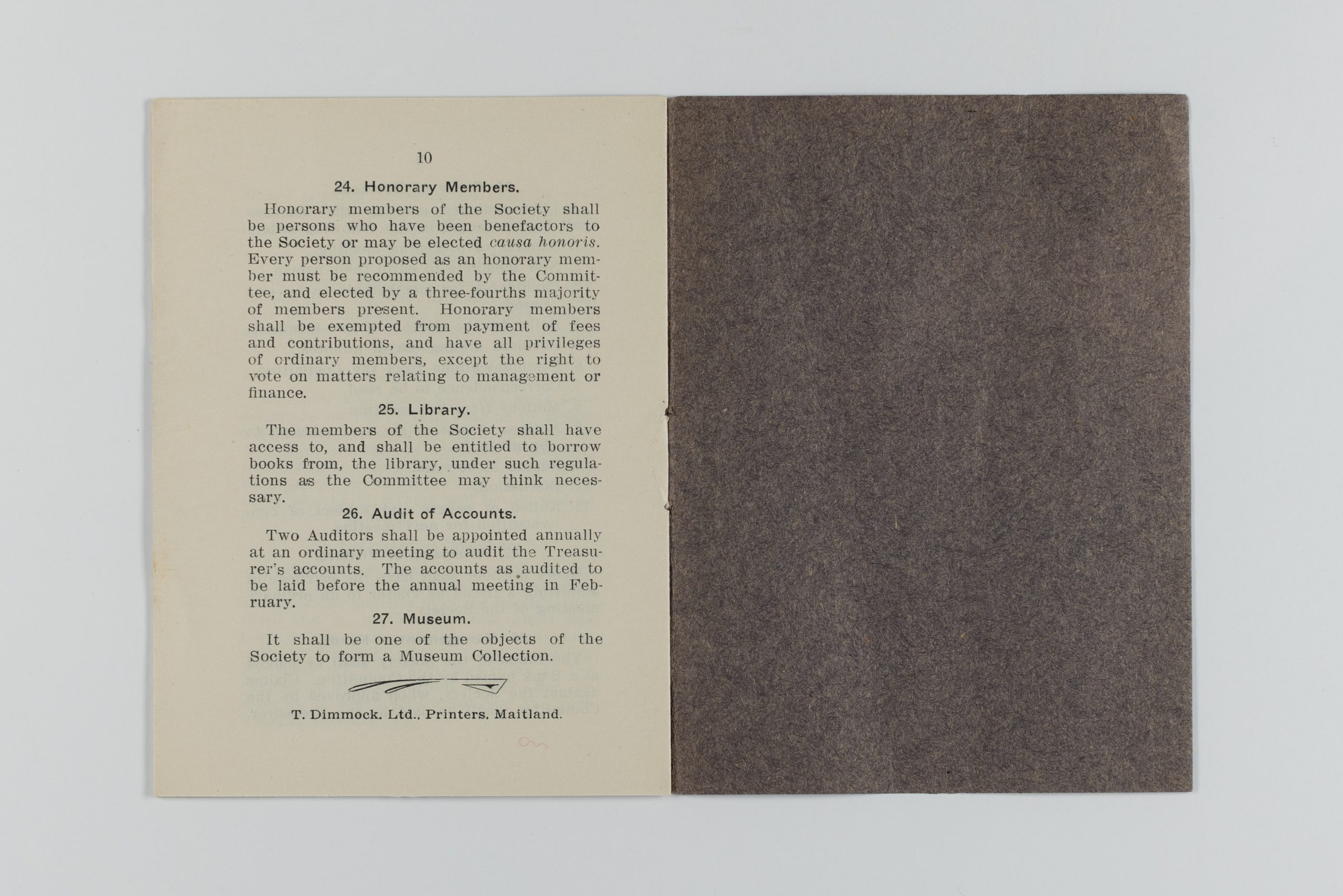 Printed book with brown cover opened to the final page. It showcases rules 24-27, including establishing honorary members, open access to the library, a yearly audit, and that an object from the society would open a museum.
