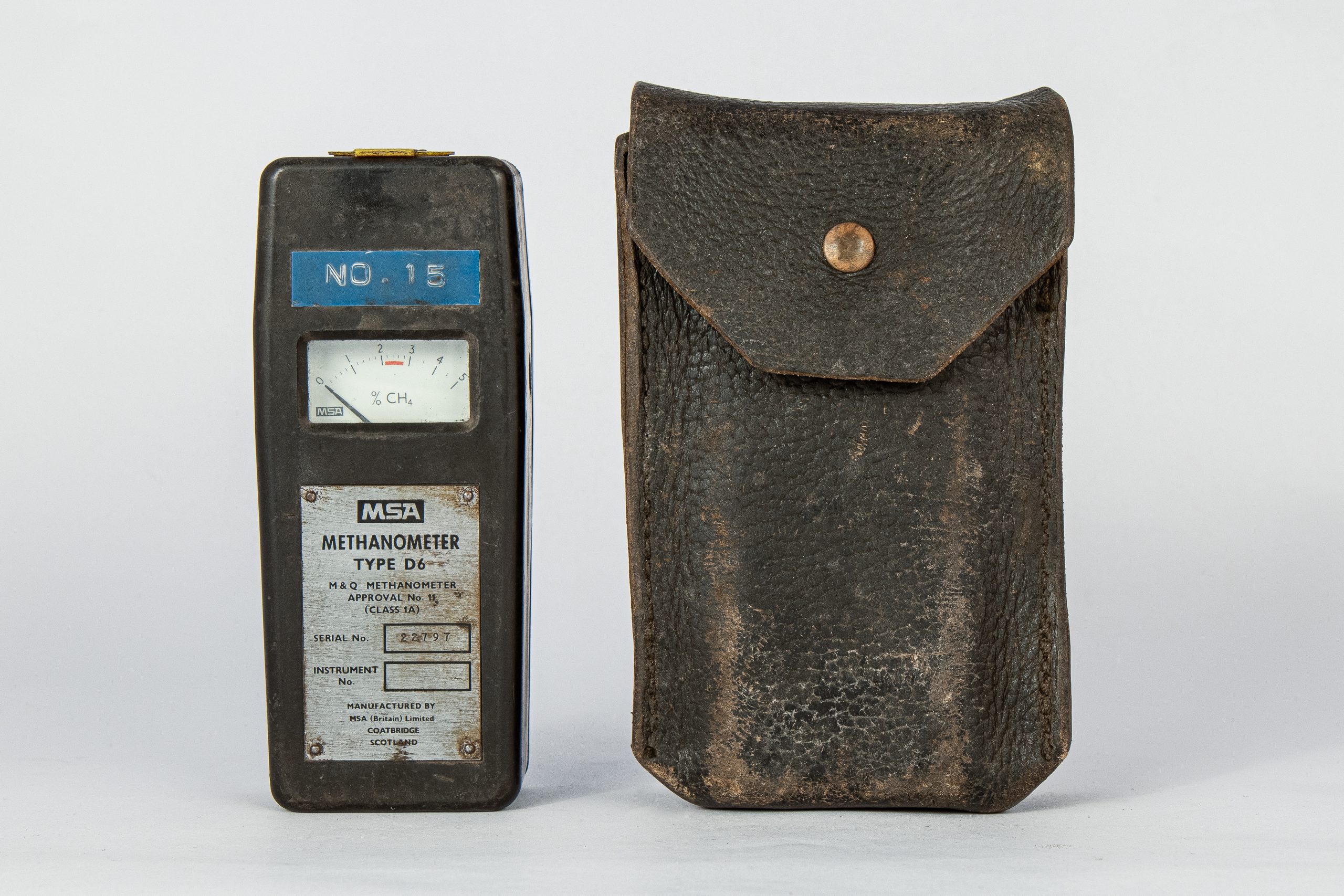 Device shaped like an old Nokia mobile phone. It has no buttons on the face but a gauge from 0-5% CH4. Panel screwed to the front reads: "MSA METHANOMETER TYPE D6. M&Q METHANOMETER APPROVAL No. 11 (CLASS 1A) SERIAL NO. 22797 MANUFACTURED BY MSA (Britain) Limited COATBRIDGE SCOTLAND." Beside it is a leather pouch to hold the device.