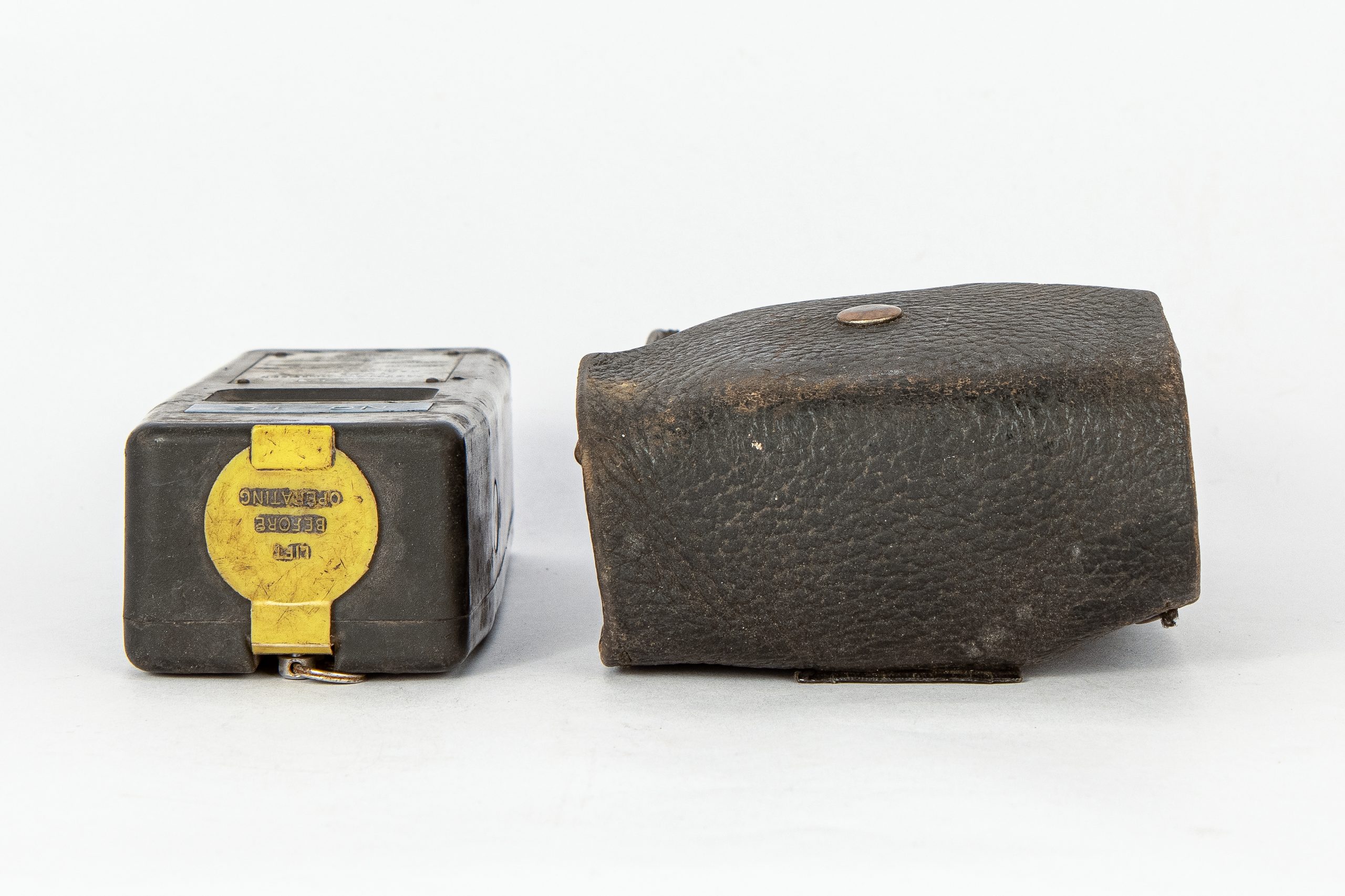 Top of device shaped like an old Nokia mobile phone. A circular, yellow panel reads, "LIFT BEFORE OPERATING." Beside it is a leather pouch to hold the device.