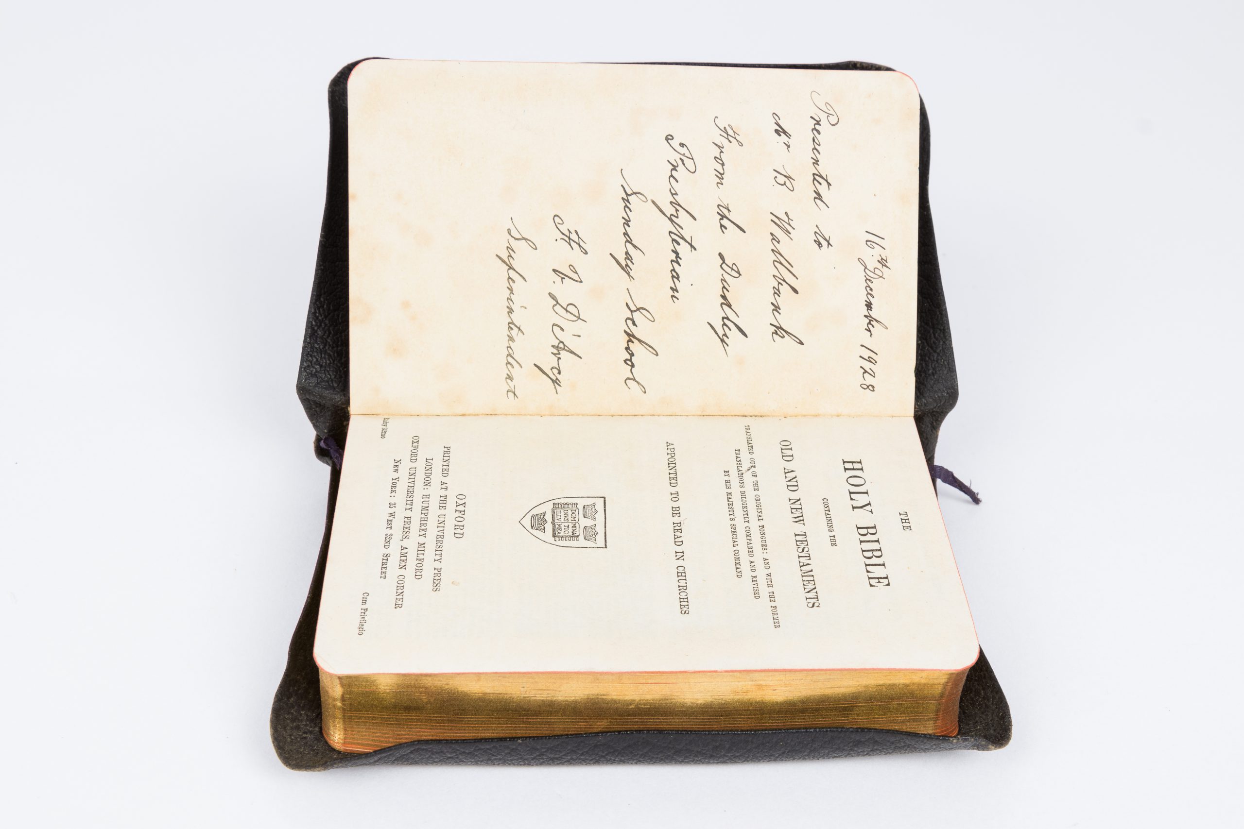Black, leather-bound bible open to the first pages, the blank page features a handwritten inscription.