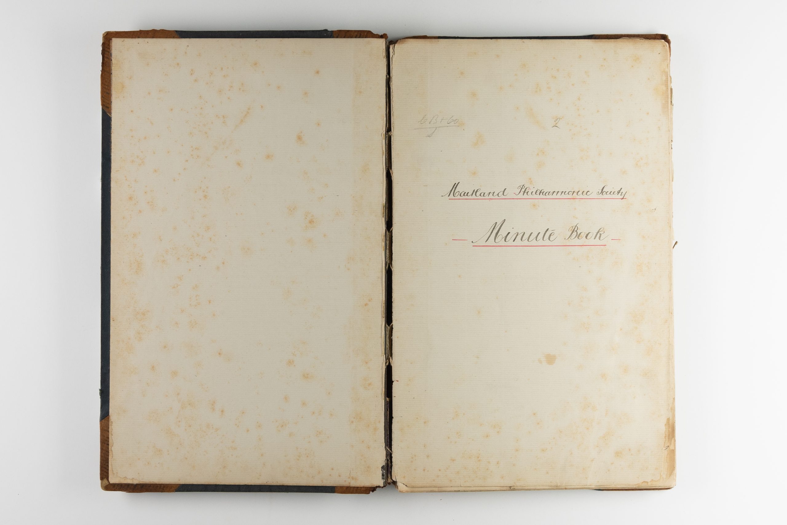 Open book with stained pages, this is the title page which reads, in handwritten cursive: "Maitland Philharmonic Society Minute Book"