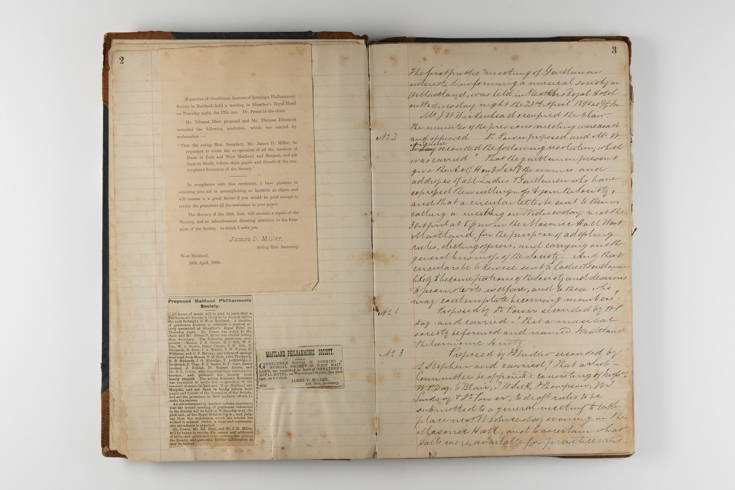 Open book with stained pages, handwritten cursive fills the right page and a few cuttings from newspapers talking about the society are stuck to the right as well as a letter from the Acting Hon. Secretary, Jamee D. Miller.