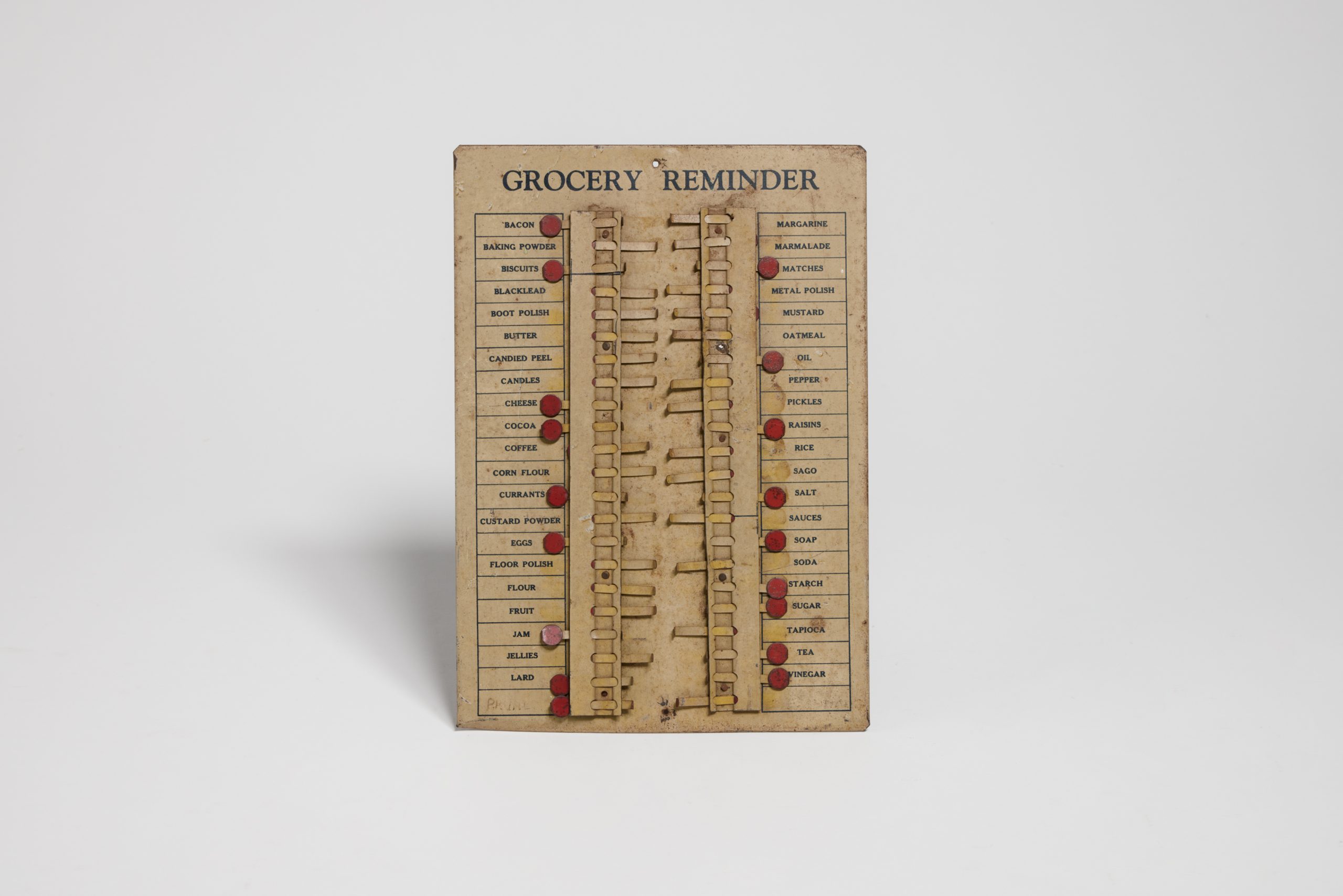 Yellowed paper "GROCERY REMINDER"; lists items like bacon, oil, and cheese; each item has a pull-out tab with a red dot to mark them