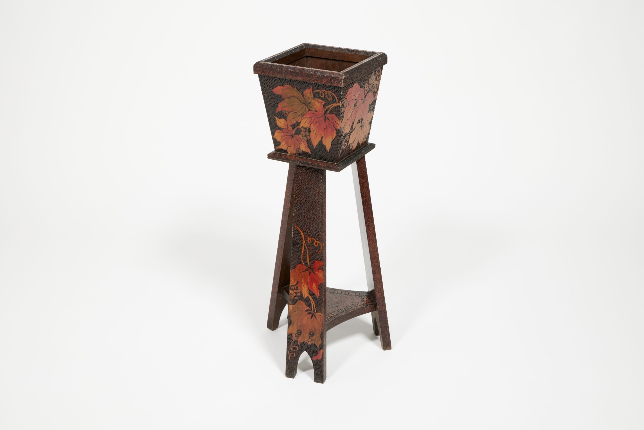 Wooden box on three, wide, wooden legs; reddish yellow design on dark wood are leaves and vines burned into the surface