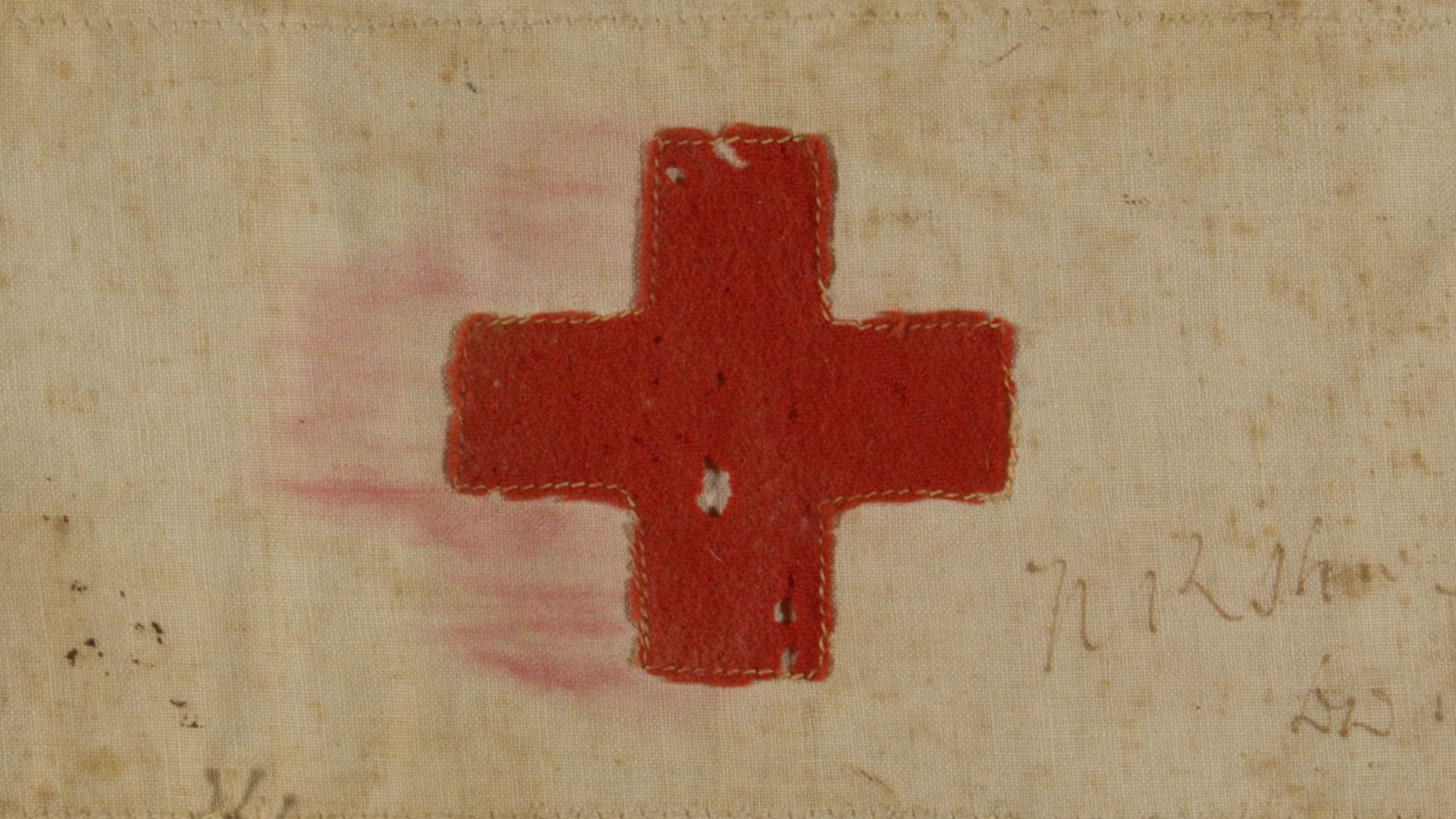 Red Cross stitched into, and staining, yellowed fabric