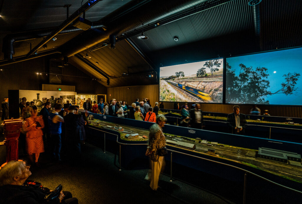 a dimly lit exhibition is well-attended, a large model train is the main object