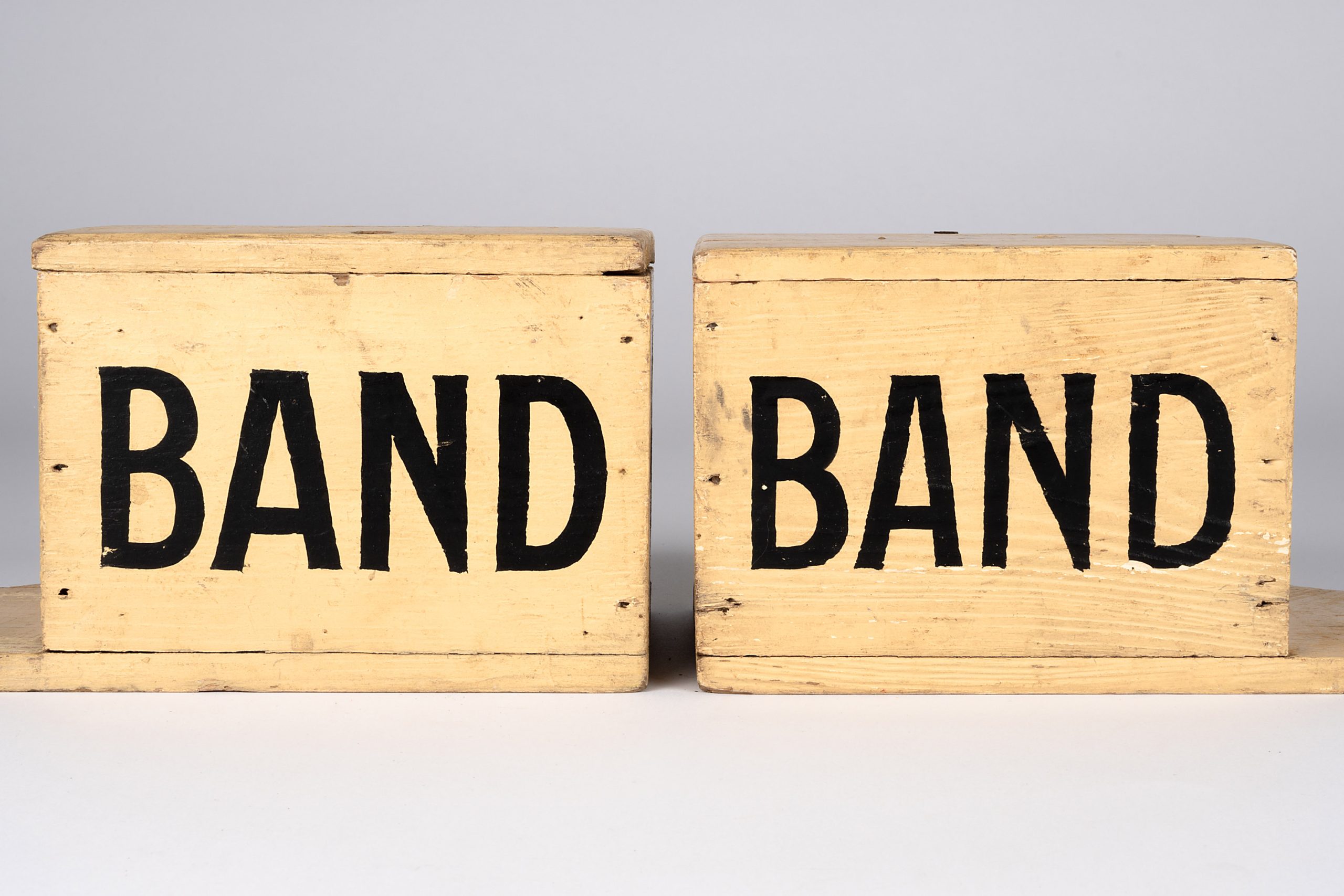 two pale, rectangular wooden boxes attached to paddle shapes which act as a handle. They are labelled "BAND"