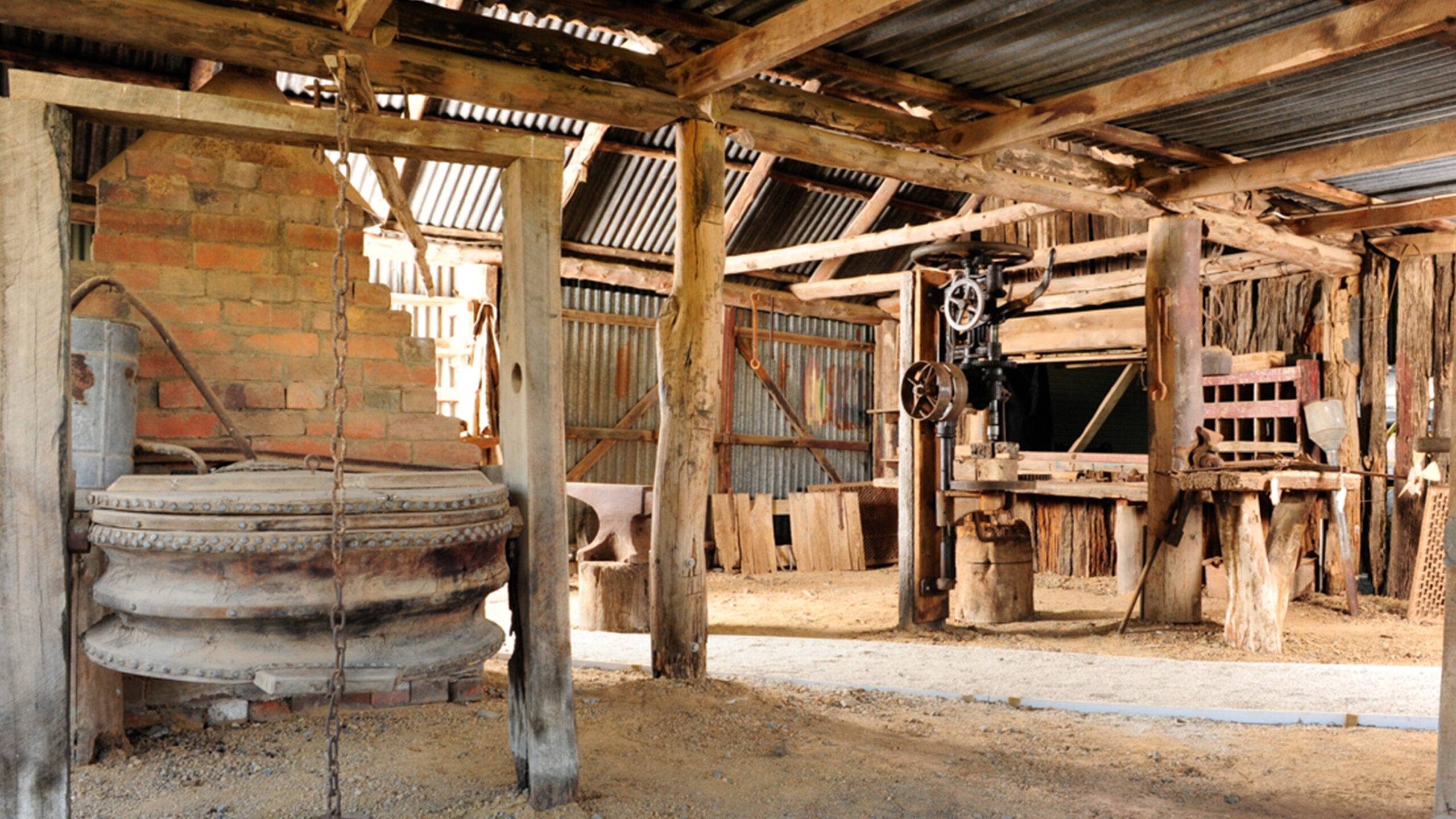 interior of a blacksmith workshop made of wood with dirt floors and corrugated roof, bellows are visible to the left