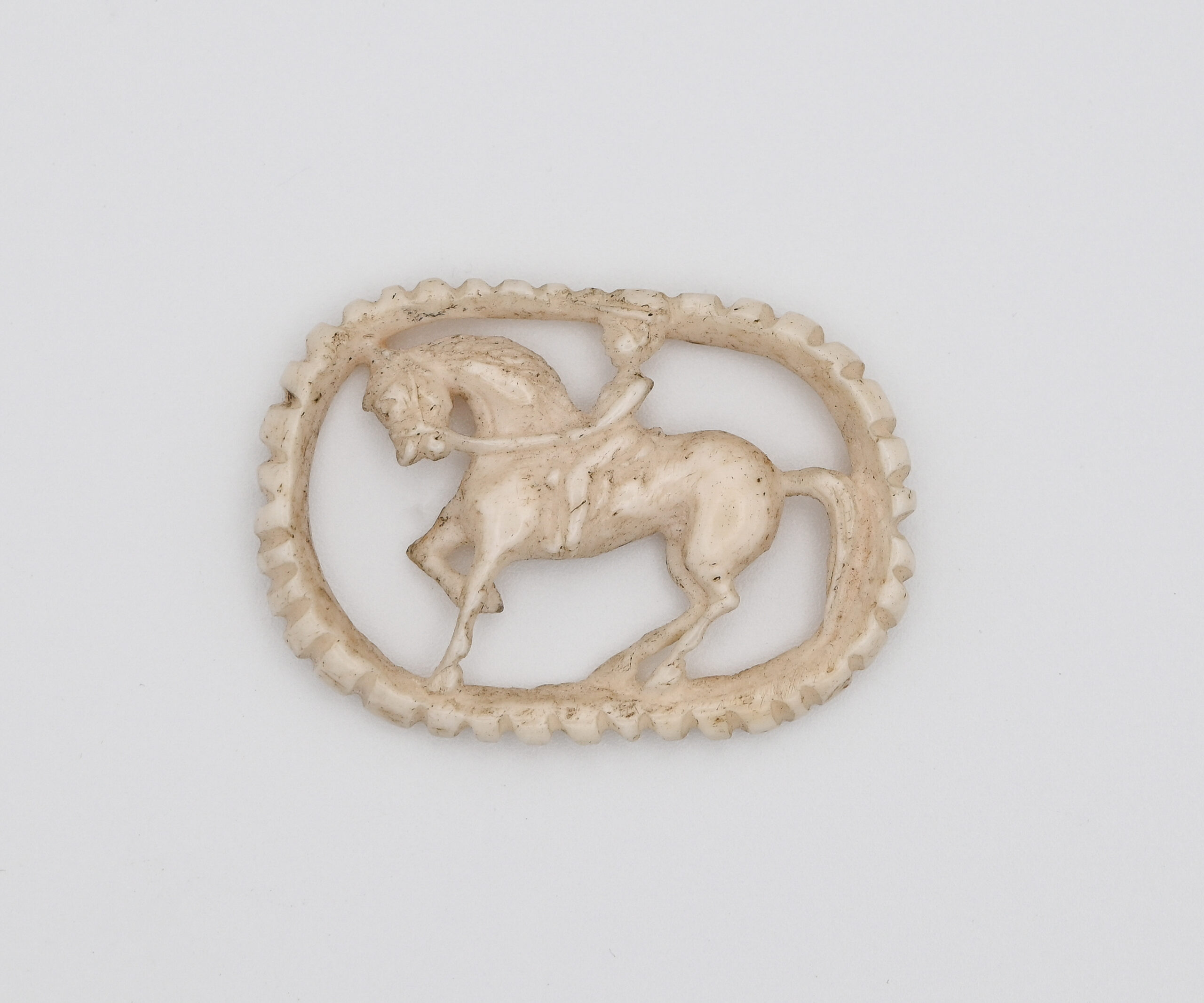 bone carved into the shape of a figure riding a horse with an oval border
