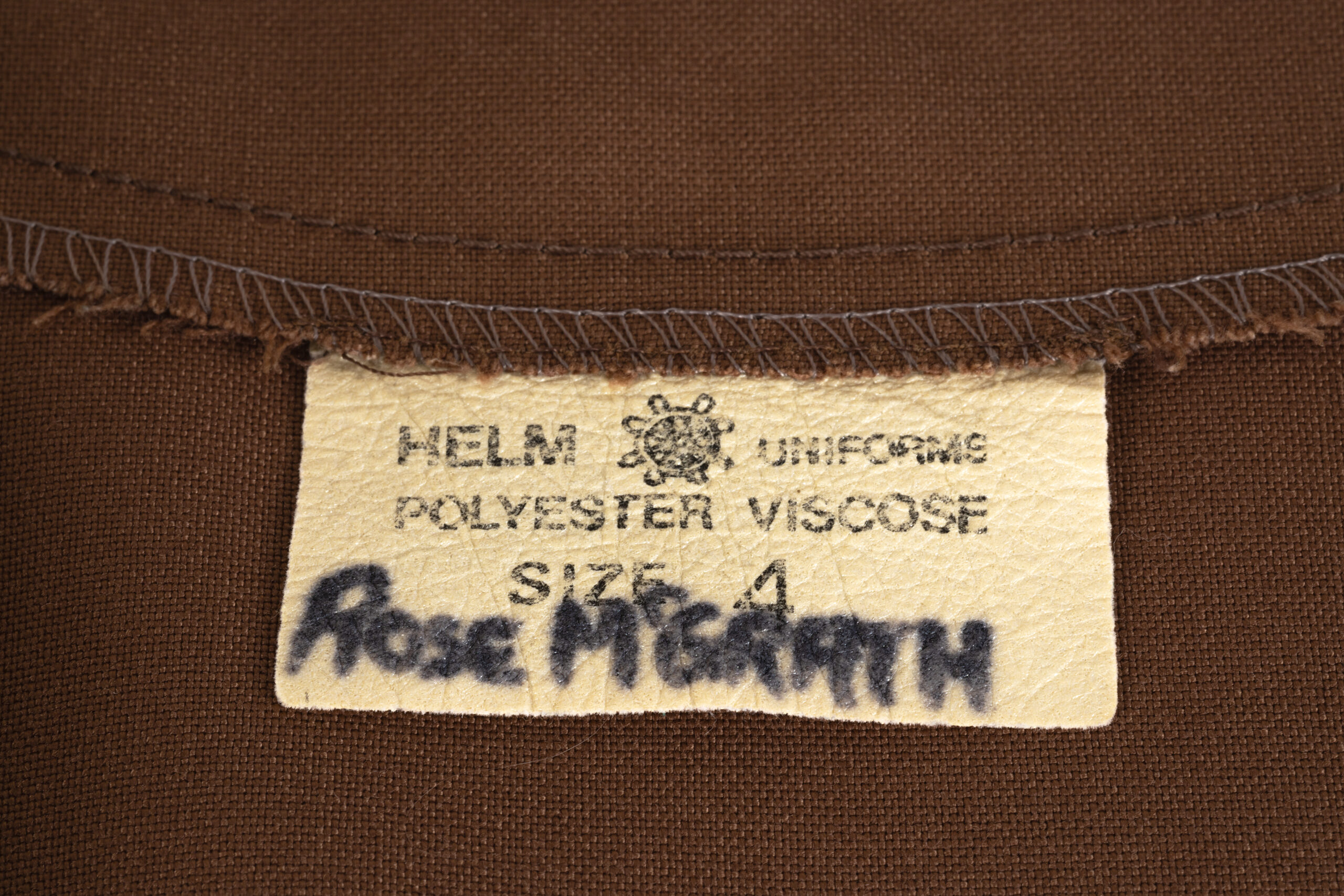 detail of tunic dress tag which reads 'HELM UNIFORMS / POLYESTER VISCOSE / SIZE 4 / ROSE MCGRATH'
